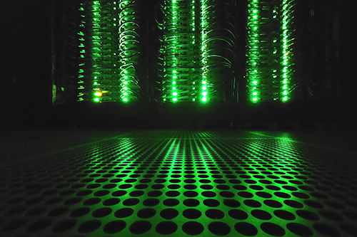 Close-up of server racks with green LED indicator lights in a dark data center.